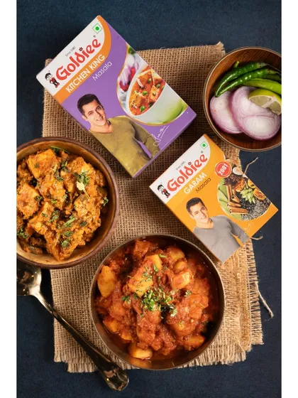 A top-down flatlay showcasing how Goldiee's Kitchen King and Garam Masala can be used in everyday Indian dishes. This visual approach helps customers see the product's versatility and imagine using it in their own cooking.