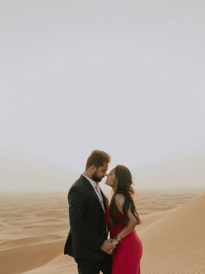 A close-up, romantic portrait of a couple about to kiss in the Dubai desert. The soft, hazy light of the setting sun creates a dreamy and intimate atmosphere.