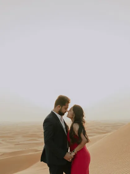 A close-up, romantic portrait of a couple about to kiss in the Dubai desert. The soft, hazy light of the setting sun creates a dreamy and intimate atmosphere.
