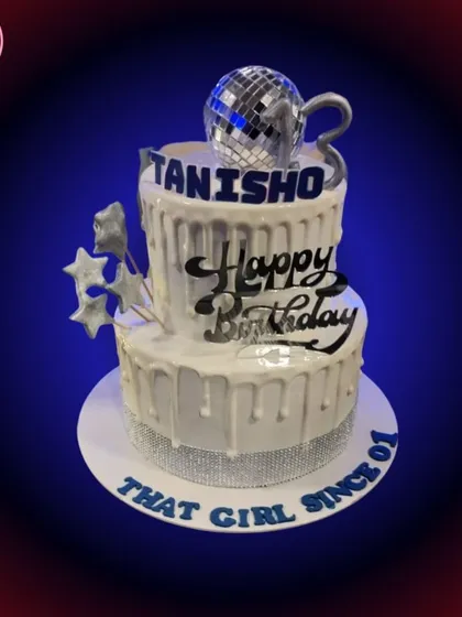 A still shot of the two-tiered disco birthday cake. The dripping white icing and rhinestone ribbon add to the glamorous party feel.
