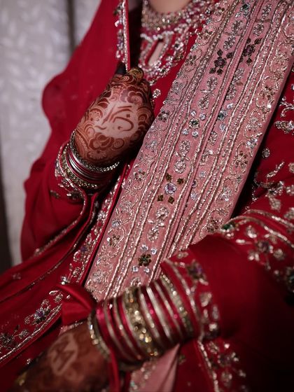 A close-up on the details of the bride's outfit and henna. The rich red fabric and silver embroidery are hallmarks of a classic Nikkah look.