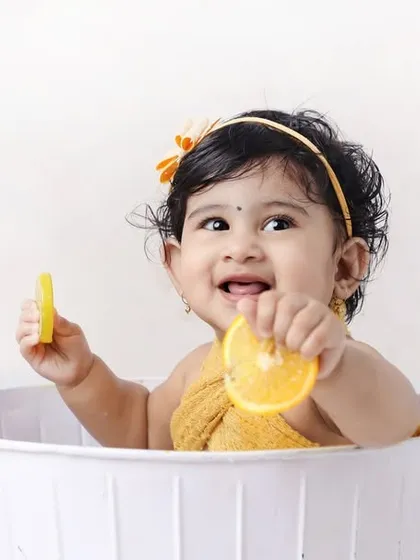 A happy baby playing with orange slices in a tub. The bright colors and cheerful expression make this a wonderfully vibrant and fun photo.