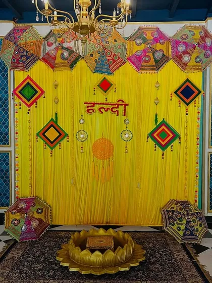 A traditional Haldi backdrop with bright yellow drapes, Rajasthani umbrellas, and colorful hangings, perfect for a classic and festive celebration.