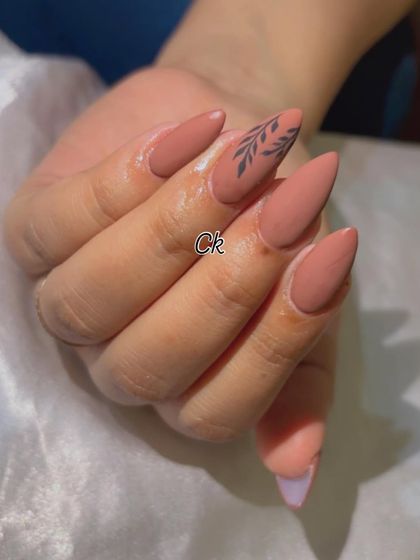 A chic and minimalist design featuring a matte nude polish with a simple, hand-painted black leaf accent.