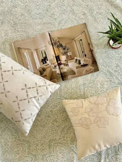 A flat-lay showcasing the textures that soothe the soul. Our geometric and floral embroidered cushions are placed on a patterned jacquard rug, highlighting the soft, pastel tones and intricate craftsmanship.