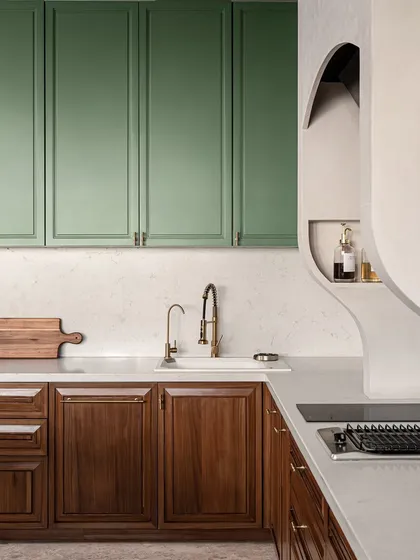 A detail of the kitchen, showing the contrast between the shaker-style sage green upper cabinets and the traditional wood-paneled lower cabinets. The brass faucet and hardware add a touch of modern luxury.
