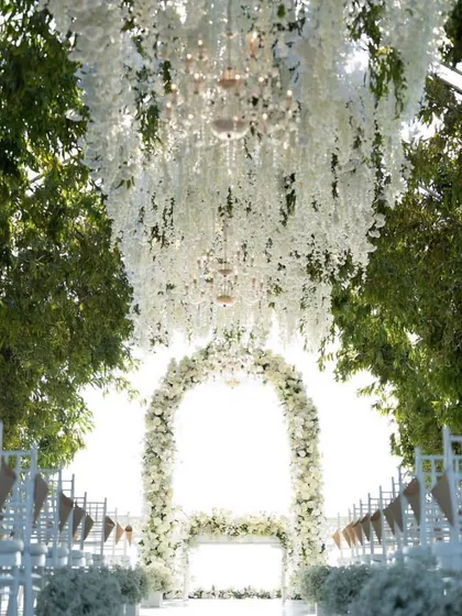 An ethereal all-white outdoor wedding ceremony, with a magnificent floral arch and a ceiling of hanging white wisteria creating a heavenly atmosphere.