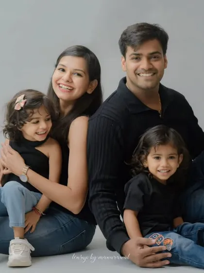 A relaxed and joyful family of four, dressed in casual jeans and black tops, smiling warmly for the camera in a clean, simple studio setting that emphasizes their connection.