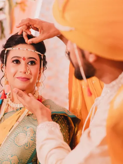 A candid moment during the wedding ceremony. The groom applies the 'tika' on the bride's forehead, a beautiful ritual where her makeup remains perfectly in place.