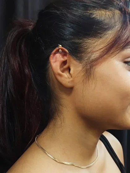 A stylish helix piercing on the upper ear cartilage, done with a gold-tone barbell. Cartilage piercings require specific aftercare, which I will explain in detail during your appointment.