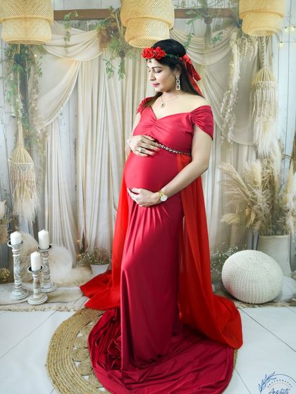 A beautiful studio portrait of a mom-to-be in a red gown with a cape and floral crown.