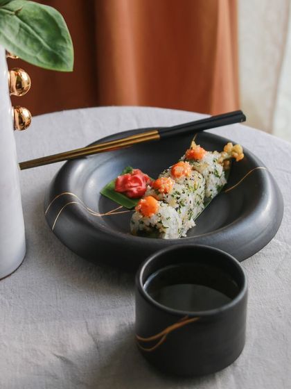 A sushi set from the 'Celebrations' collection, with a black plate and matching cup, highlighting the versatility of the elegant dinnerware.