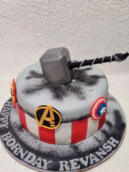 An Avengers-themed cake for a true superhero fan. This design features Thor's hammer Mjolnir crashing into the cake, surrounded by the logos of Captain America and the Avengers.