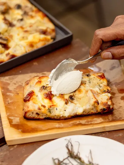 A slice of our Bianco Romana pizza being topped with a generous dollop of fresh ricotta cheese.
