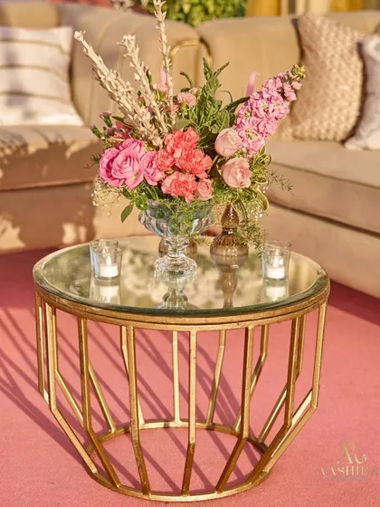 A close-up of a gold-framed coffee table, holding a beautiful arrangement of pink roses and baby's breath, with the soft glow of candles beside it.