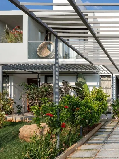 A view of the shaded walkway and private sit-outs at the SAMAM House. A metal pergola structure supports climbing plants, creating a green, living canopy that cools the space and enhances the connection to the garden.