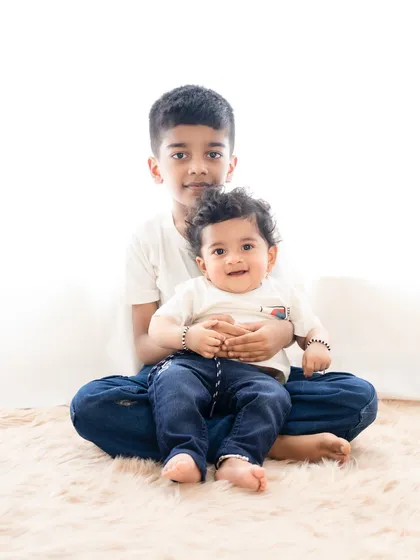 A gentle and loving portrait of two brothers. The older brother sits with his arm around the younger one, showcasing his protective and caring nature.