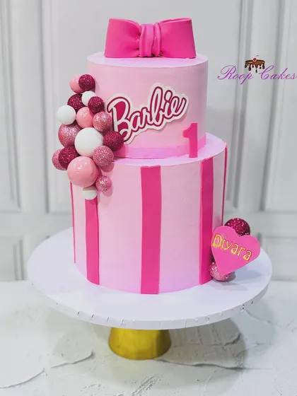 One year of magic and sweetness. This two-tier Barbie cake is perfect for a little princess's first birthday, with pink stripes, a big bow, and lots of sparkle.