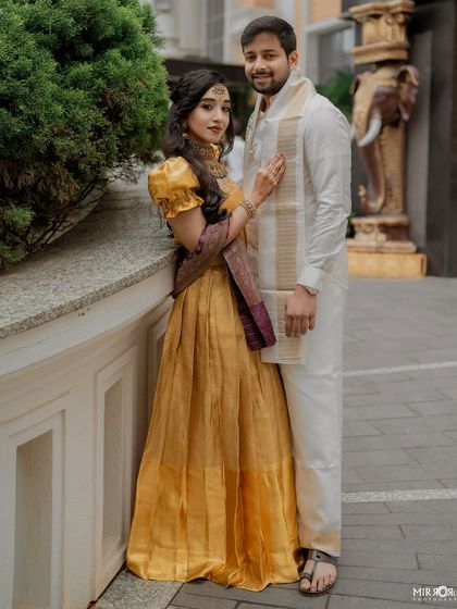 The couple together, showcasing a coordinated look for their event. The bride's golden gown is complemented by the groom's traditional white and gold attire.