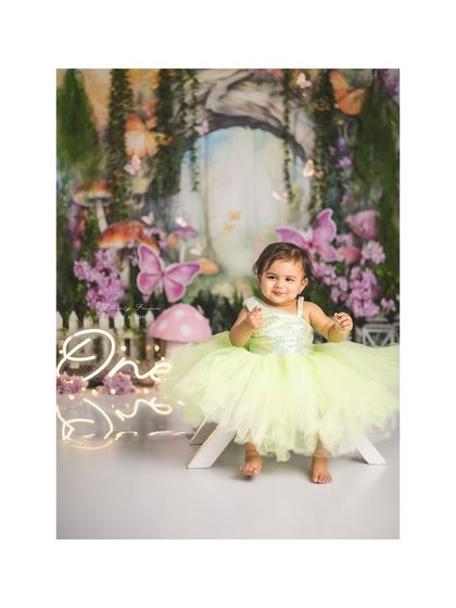 A happy little fairy in a lime green dress, sitting on a white bench in her enchanted forest.