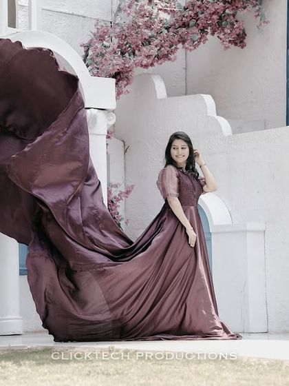 A solo portrait of the bride-to-be, her mauve trail gown caught in motion, set against a beautiful white architectural backdrop with pink flowers.