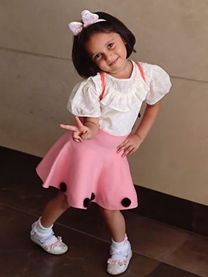 Striking a pose in a cute and casual two-piece look. The ruffled white top pairs perfectly with a pink skirt featuring fun black polka dots at the hem.