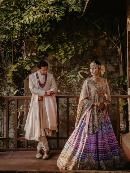 A beautifully composed portrait on a rustic balcony. The bride's colorful Tarun Tahiliani lehenga stands out against the natural textures of the wood and stone.