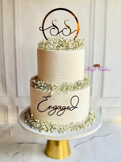 A simple yet stunning two-tier engagement cake. The clean lines of the white buttercream are beautifully accented with delicate baby's breath and elegant black script toppers.