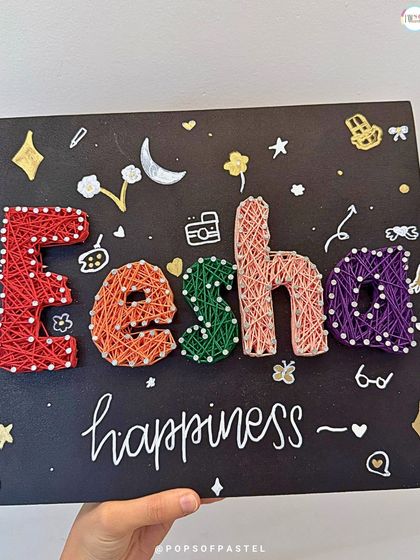 A close-up of a finished, personalized string art name board, showcasing vibrant colors and fun, hand-drawn embellishments.