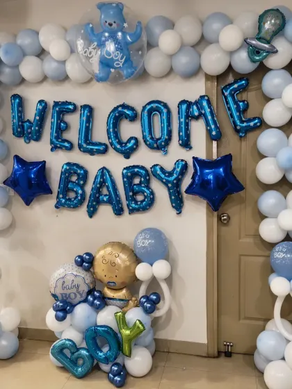 A classic 'Welcome Baby' decoration for a baby boy. The setup includes a full balloon arch, 'WELCOME BABY' and 'BOY' foil letters, and baby-themed foil balloons.