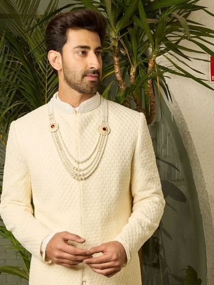 This shot captures the regal bearing of the off-white sherwani. The textured fabric and perfect fit create a silhouette that is both traditional and modern.