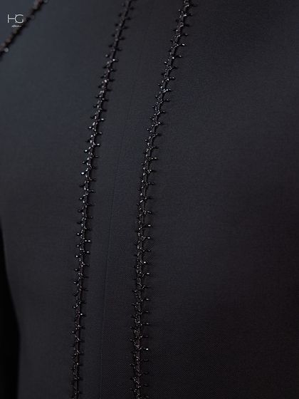 A close-up of the delicate, hand-stitched beading that runs down the back of the achkan, adding a hint of sparkle to the deep black fabric.