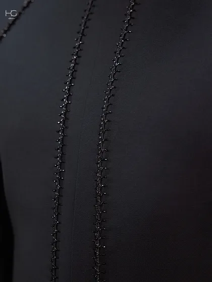 A close-up of the delicate, hand-stitched beading that runs down the back of the achkan, adding a hint of sparkle to the deep black fabric.