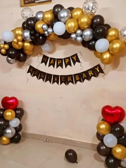 A simple balloon arch decoration for an at-home anniversary celebration. This setup uses black, gold, and silver balloons with a "Happy Anniversary" banner, perfect for decorating a living room wall.