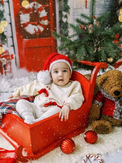 A baby in a red sleigh, looking calm and sweet. A beautiful, postcard-perfect holiday photo.