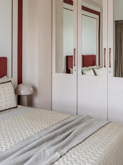 This bedroom combines a bold, quilted headboard in deep red with vertically striped wallpaper and mirrored wardrobe doors, creating a dynamic interplay of color, pattern, and reflection.
