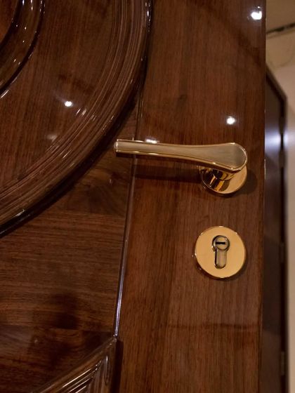 A close-up of a high-gloss solid wood door, showing the flawless finish and the classic gold hardware.