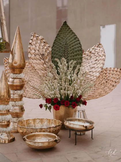 A close-up of the decor, showing brass urlis, woven palm leaves, and tuberose arrangements.