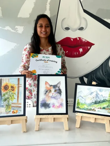 A student proudly holds her certificate alongside her three beautiful watercolor paintings.