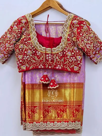 A stunning Kanchi Pattu saree in a soft lilac, paired with a contrasting red blouse. The blouse is the highlight, featuring incredibly dense and heavy maggam work embroidery on the neckline and sleeves for a bridal-quality finish.