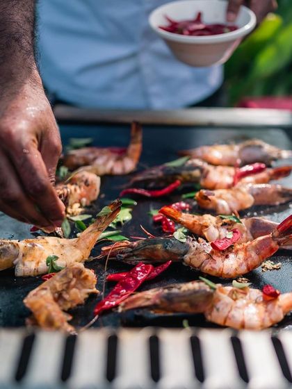 A chef prepares succulent grilled prawns on a hot plate during our anniversary brunch, showcasing the fresh and flavorful live cooking stations.
