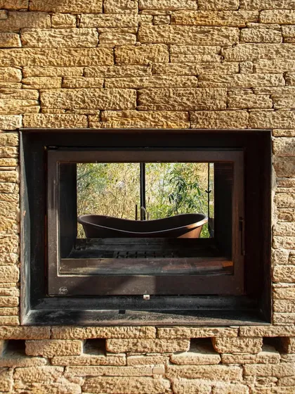 A window at the Himalayan home frames a view of an outdoor bathtub, blending the intimate act of bathing with a direct connection to the rugged, natural setting.