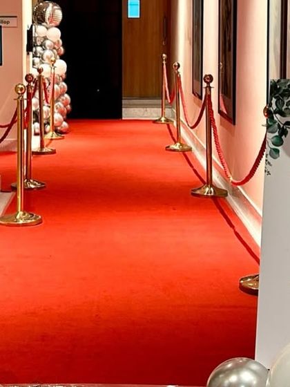A red carpet entrance for a glamorous 18th birthday party. Silver and white balloon pillars and a welcome sign complete the VIP experience.