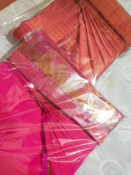 Two sarees, one pink and one orange, packed in clear plastic to keep them dust-free after folding.