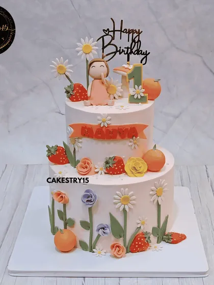A sweet two-tier tiramisu cake with an autumn floral and fruit theme. This 4kg cake is decorated with fondant strawberries, daisies, and a cute girl topper for a first birthday.