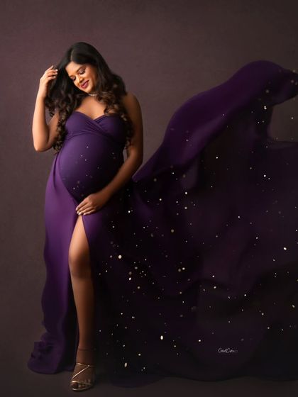 A quiet, beautiful moment. The mom-to-be looks down at her bump, her purple gown sparkling with a magical dust effect.