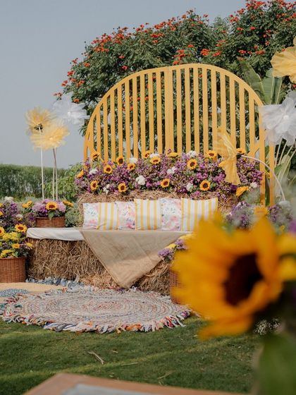 A detailed shot of the rustic Haldi seating, featuring a hay bale sofa with striped cushions, a colorful rug, and giant paper flowers.