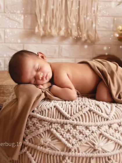 A beautiful shot of a baby sleeping on a woven macrame pouf. This pose highlights the baby's delicate features against the detailed, textured surface.