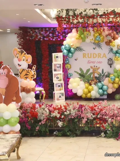 A beautiful shot of the stage setup for Rudra's first birthday. The combination of a flower wall, a custom jungle backdrop, and adorable animal cutouts creates a rich and festive look.