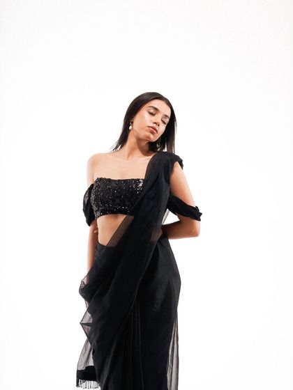 A minimalist, high-key studio shot of a modern black saree. The clean white background makes the sequined blouse and sheer fabric stand out, creating a chic and contemporary ethnic look.
